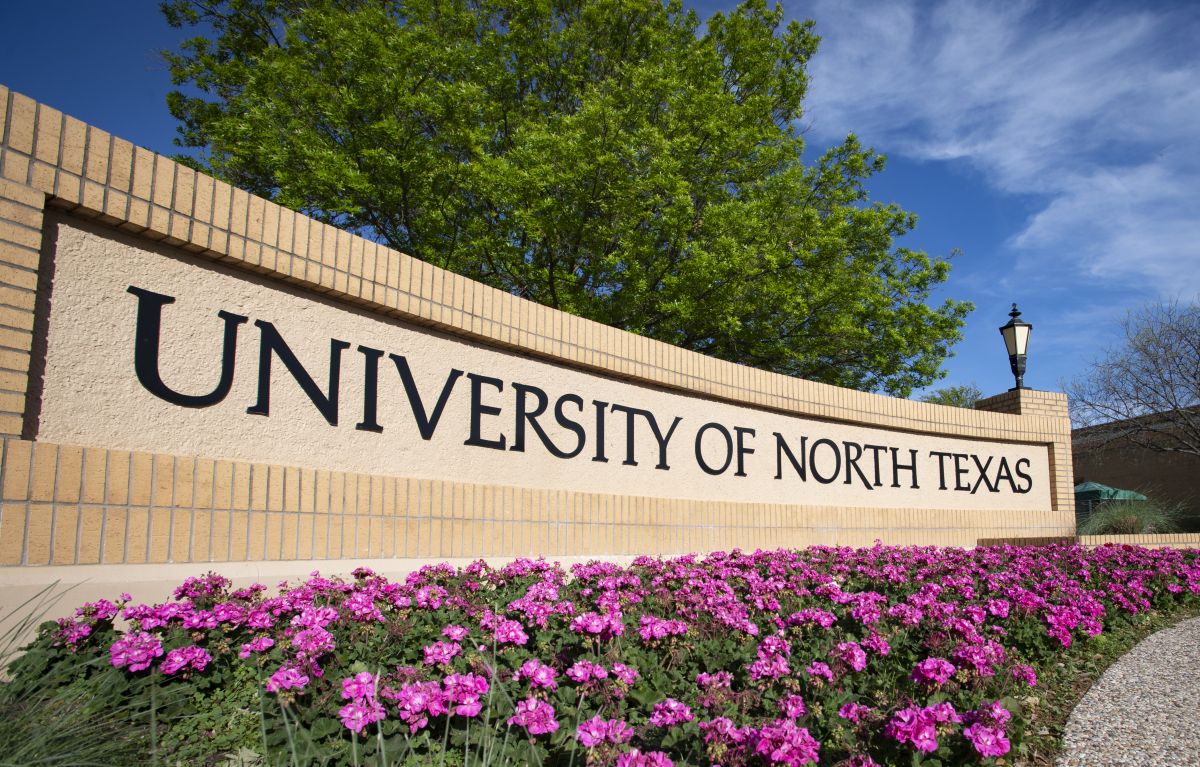 Picture of University of North Texas sign surrounded by trees and purple flowers