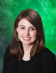 Picture of Staff Senator Julie Elliott. Julie is smiling and has shoulder-length brown hair with a silver earrings and black long-sleeve shirt against a green background