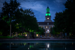 University building with a pool in the front and the tower lit with the color green