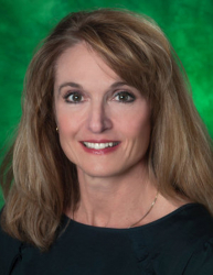 Picture of Staff Senator Kristi Klusman. Kristi has shoulder-length blonde hair, hazel eyes and red lips. Kristi is smiling and is wearing a black top against a green background