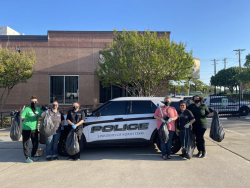 Picture of six UNT dispatchers with trash bags in front of UNT Police Department white SUV
