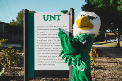 Picture of Scrappy pointing to UNT We Mean Green sign